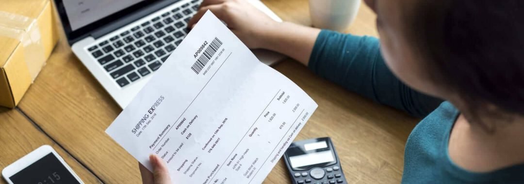 una mujer revisando facturas con una calculadora y un ordenador