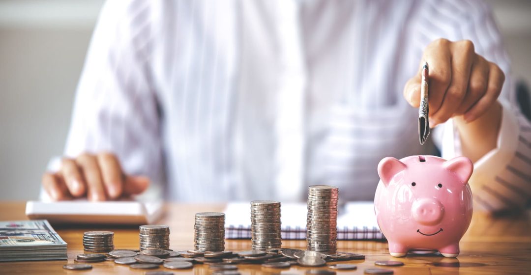 Una persona haciendo cálculos e introduciendo monedas en una hucha