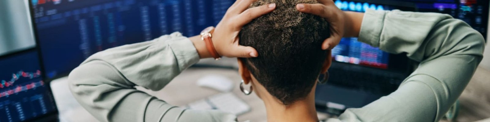 Una mujer mirando pantallas con gráficos y con las manos en la cabeza